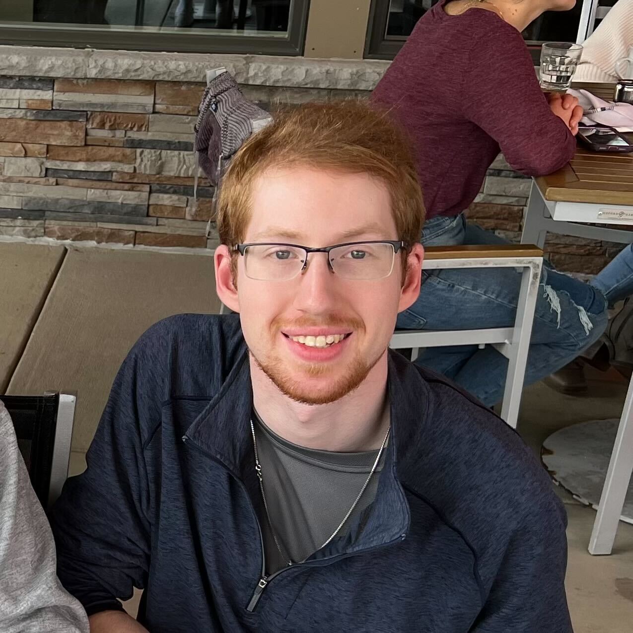 A photo of Erik Mechtel, seated indoors, smiling, wearing glasses and casually dressed.