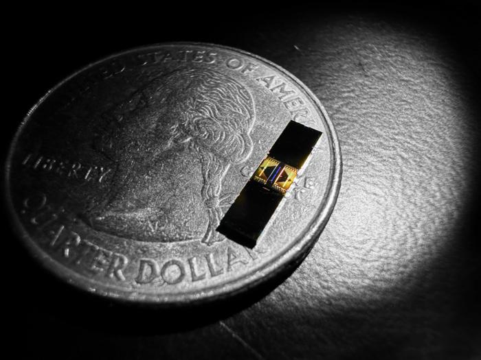 A metallic rectangular chip rests on a quarter beside the image of George Washington's profile. 