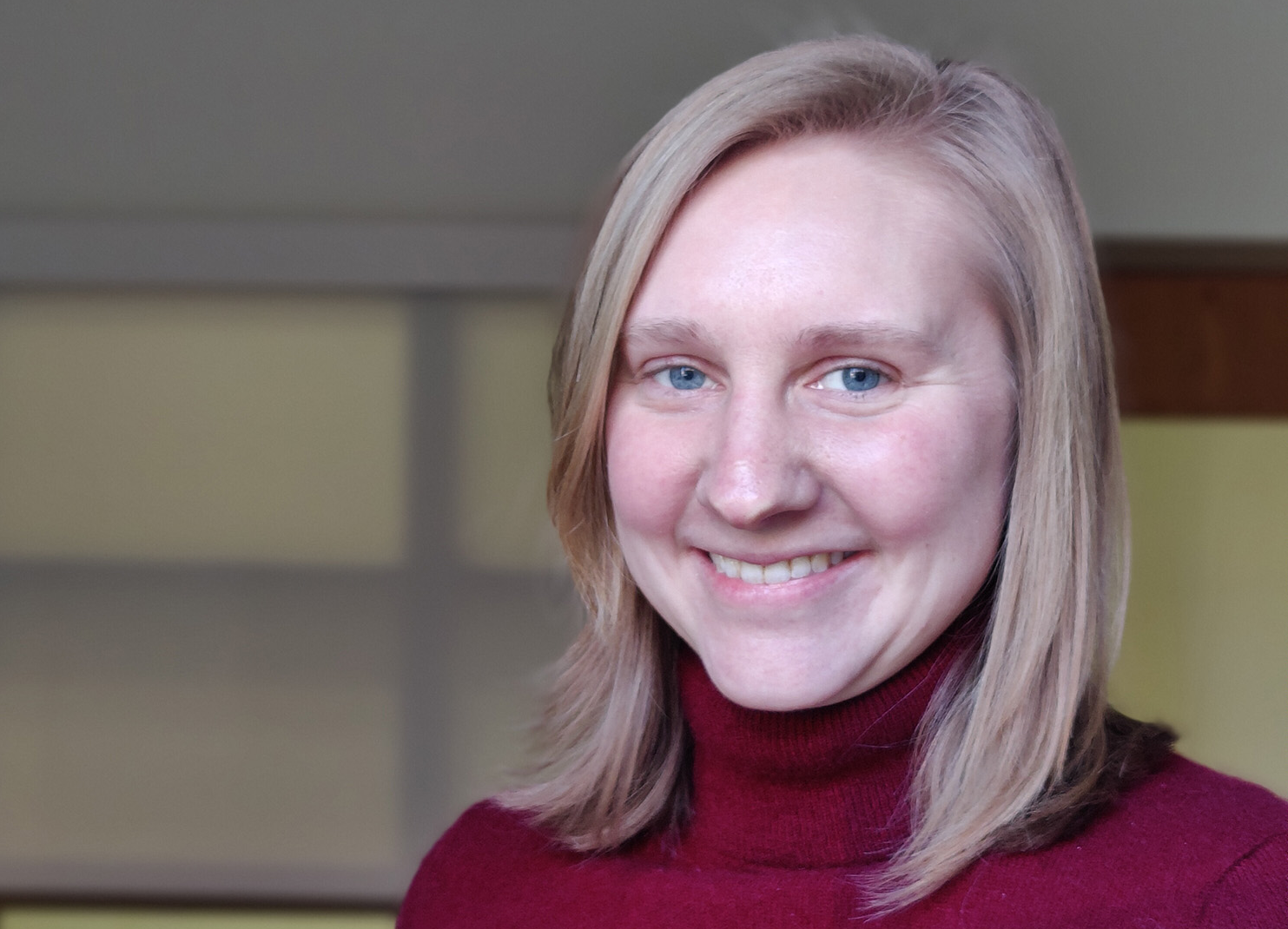 a woman smiling at the camera and wearing a red turtleneck