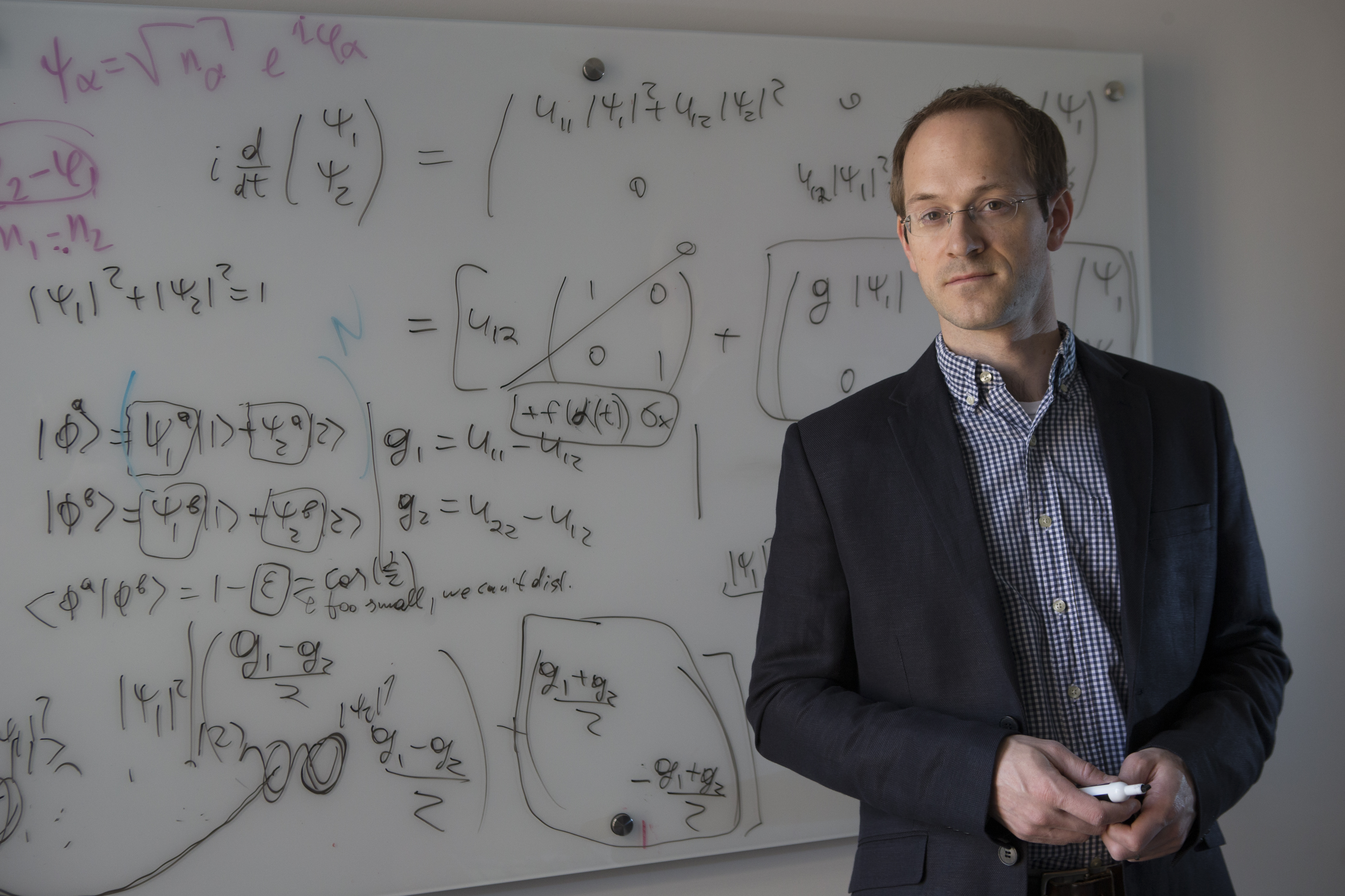 A photo of Andrew Childs standing in front of a whiteboard covered with numerous handwritten equations. 